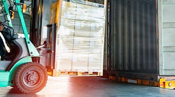 Forklift driver unloading shipment product pallet into container