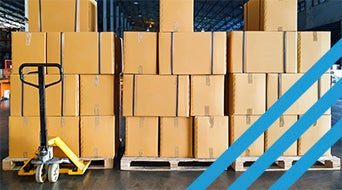 Stacks of brown cardboard boxes on wooden pallets in a warehouse. A yellow hand pallet truck is positioned in front of the boxes. Blue diagonal lines are overlaid on the right side of the image.