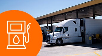 A white semi-truck parked under a fuel station canopy on a sunny day. An orange circle with a white fuel pump icon is overlaid on the left side of the image.