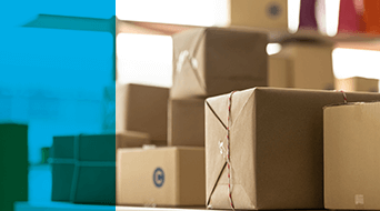 A pile of variously sized cardboard packages stacked on a surface, ready for small business shipping. The left side of the image features a blue overlay. The blurred background hints at an indoor setting, possibly a bustling warehouse or office environment.